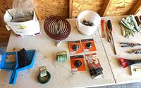 Overall table view with dustpan, edging coil, packaged spools, wire, pail, pruning shears and misc.