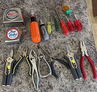 Group overview of all tape measures, screwdrivers and pliers on countertop