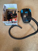 Canister vacuum with hose beside box of accessories