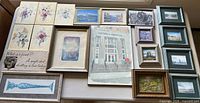 All framed artworks laid on table, showing variety and quantity