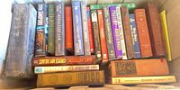 Books stacked in cardboard showing spines including John Sandford, Robert B. Parker, Hamlet, The Golden Orange etc.