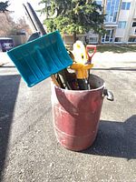 Tools gathered in barrel showing snow shovel blade, pitchfork handle, blower tube