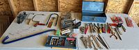 Wide view of all tools arranged on table including pry bar, planes, saws, staplers, wrenches and toolbox
