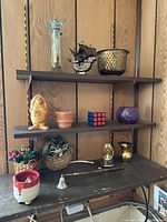 full view of shelving with mixed décor items including metal ship, brass bowl, glass vase, figurine, terracotta pot, Rubik's cube, purple bowl