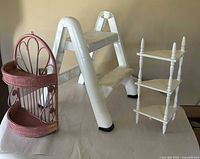 Group view of white plastic step stool, pink wicker corner shelf, white wooden corner shelf
