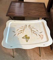 Overview of cream decorative tray in front, brown woodgrain tray behind, both with folded legs extended
