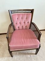 Front view of pink upholstered armchair showing tufted back, cushion, cane sides