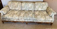 Front view of three-seat sofa showing full carved wood base and floral upholstery