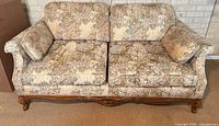 Front view of sofa showing floral upholstery, two seat cushions, bolster pillows and carved wood base