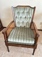 Front view of armchair showing green striped upholstery, button-tufted back, cane sides, wood frame