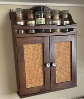 Front view of closed wall-mounted wood spice cabinet with jars on open top shelf
