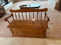 Full view of wooden storage bench showing spindle back, arms, lid closed
