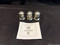 Front view of three matching electroplated spice shakers with MaxSold lot card