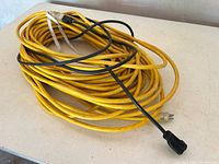 Coiled yellow heavy duty extension cord with integrated ribbon tie and black extension cord overlay