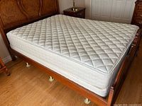 Overall view of mattress on wooden bed showing quilted pillow-top surface, box spring beneath, and metal frame feet visible