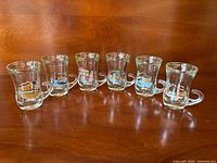 All six glass espresso cups lined up showing front graphics and shape