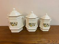 front view of three graduated ceramic canisters with lids showing pear and daisy decal