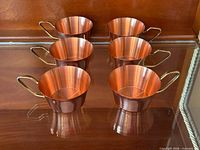 Six copper-tone cups in cabinet