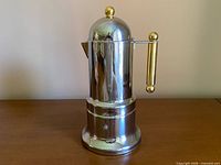 Full view of stainless steel moka espresso maker with gold-tone handle and finials