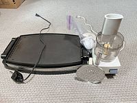 Electric griddle with power cord, food processor assembly with pusher and slicing/shredding disc displayed on carpet
