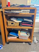 Front view of oak rolling desk cart showing pull-out shelf, open shelves, caster wheels and included office contents