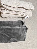 Folded beige quilted blanket and gray microfiber throw on carpet