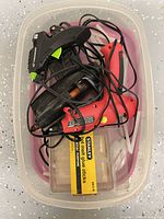 Top view of all items in clear bin: three corded glue guns, Stanley glue stick pack, loose sticks