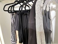 Assorted tops on hangers showcasing black-white striped cardigan, black cardigan, grey tank, black camisole