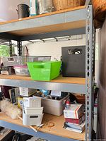Front view of gray metal shelving unit with three MDF shelves holding assorted bins and baskets
