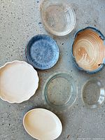 Top view showing seven ceramic and glass items: two clear pie plates, oval glass baker, cream fluted tart dish, blue plate, beige oval platter, blue-rim beige swirl bowl