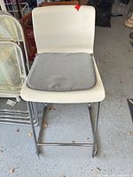 Front view of stool showing white molded seat, gray cushion, chrome frame