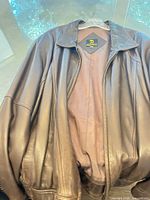 Front view brown leather jacket on hanger showing lining and tag