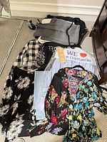 Pile of garments showing trousers, plaid shirt, floral items, striped shirt in dry-clean bag, hangers