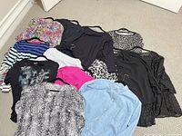All eleven assorted women’s tops and blouses arranged on floor showing patterns, colors and styles