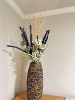 Full view of woven rattan floor vase with floral insert