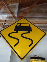 Front view of yellow diamond road sign with black skid-mark car graphic
