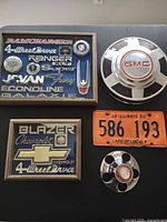 Overall lot showing both framed emblem displays, GMC hubcap, license plate, center cap