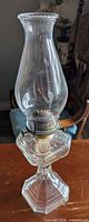 Full view of oil lamp showing glass chimney, metal burner, glass base