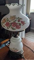 Full view of lamp showing milk glass shade, floral design, brass fittings, cord