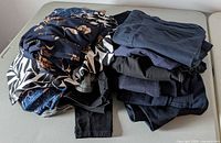 Stack of assorted pants and jeans on table, showing colors and patterns