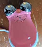 Front view of pink NuFACE device showing chrome spheres and power button