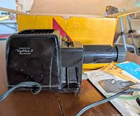 Left side view of projector showing model name, power cord, box and instructions
