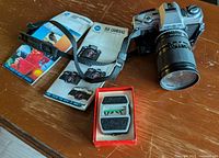 Camera with attached lens, strap, manuals and light meter set on table