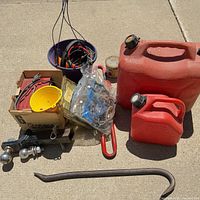 Overview of lot: gas cans, hitch, pry bar, charger box, bucket of straps
