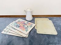 Stack of six placemats showing both floral bouquet and scalloped rose designs with ceramic pitcher for scale