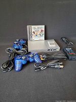 Front view of PS2 Slim console, two blue controllers, cables, Final Fantasy IX game