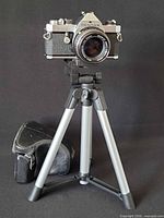 Front view of Pentax MX camera with lens on mini tripod, Canon case beside