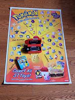 Poster laid flat with handheld game and tin placed on lower section