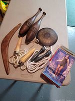 All items laid out: two wooden Indian clubs, wooden boomerang, metal discus, two jump ropes, AMF Whitely box