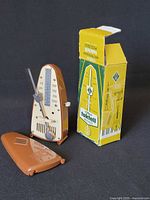 Metronome with cover removed beside original box